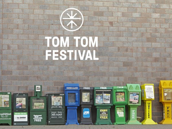 Newspaper boxes lined up against a wall, with the Tom Tom Festival logo