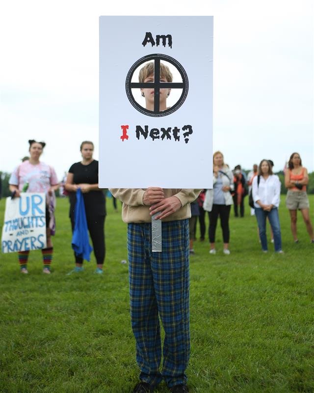 a young protestor behind a sign that says "Am I Next?"