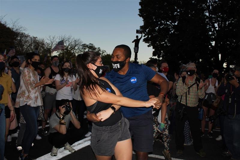 two people dancing in the street with black medical masks that say "Vote"